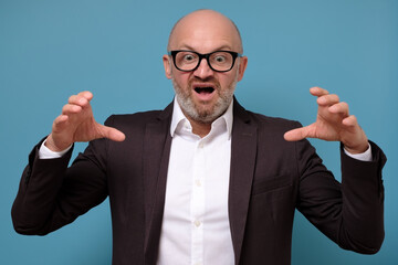 aggressive mature italian man in glasses posing isolated on blue wall.