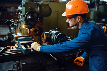 Worker in uniform and helmet works on lathe, plant