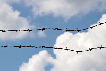 Silhouette of barbed wire on background of blue sky and white clouds. Concept of boundary, prison or quarantine