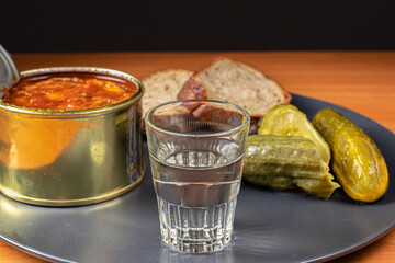 Drinks and snacks. A glass of vodka, sprats, bread and pickles.