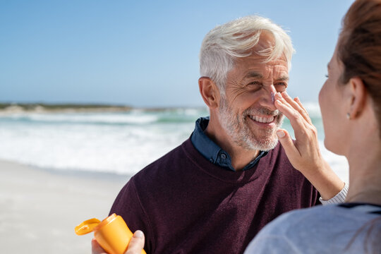 Woman applying sunscreen on senior man nose