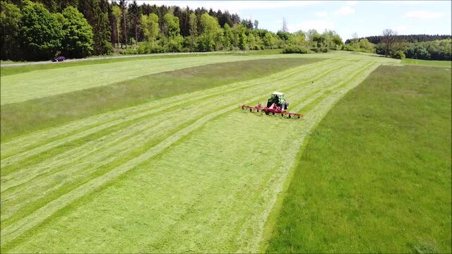 Bauer f&auml;hrt mit dem Traktor auf dem Feld und wendet das Heu