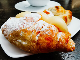 One small croissant with vanilla cream and cheese pastry with chocolate pieces served in white plate with black filtered coffee for a traditional greek breakfast