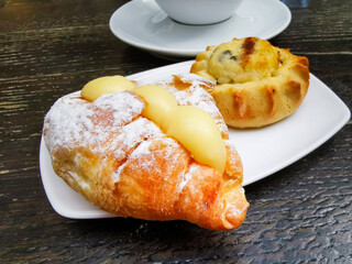 One small croissant with vanilla cream and cheese pastry with chocolate pieces served in white plate with black filtered coffee for a traditional greek breakfast