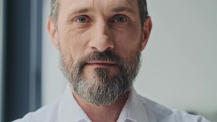 A close-up view of a calm mature man is opening his eyes and looking to the camera while standing in the office - Powered by Adobe