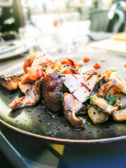 Grilled mixture of mushrooms with grilled Cretan goat cheese cooked with little onions, thyme and mushrooms cream served on black ceramic plate