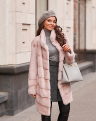Beautiful caucasian woman with long brunette hair in pink fur coat and gray beret walking in city....