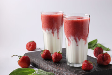 Two servings of homemade smoothies with fresh strawberries, mint and yogurt in glasses on white...