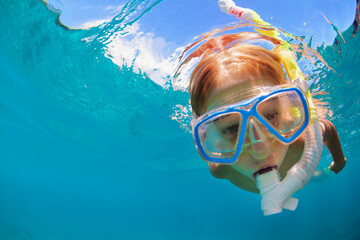 Happy little kid in snorkeling mask and wetsuit jump and dive underwater in coral reef sea lagoon. Family travel lifestyle in summer adventure camp. Swimming activities on beach vacation with child.