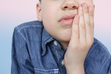 kid, a schoolboy holds his hand on the lower jaw, wrinkles from toothache, the concept of pediatric dentistry, treatment of teeth, oral care