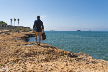 Man walking along the coast with a Spanish guitar in his hand