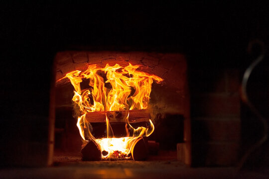 A fire flares up in the firebox of a Russian stove. Live fire in the furnace of the Russian stove, on the right is a metal gate with a figured handle, in the foreground is a stove.