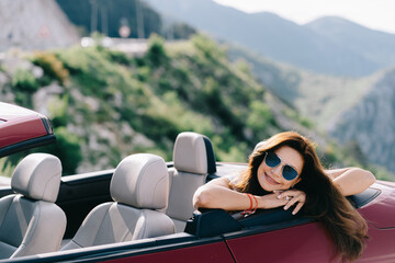 Happy woman sits in a red convertible car with a beautiful view