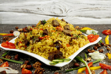 Pilaf is a traditional oriental dish of meat and rice. On a white square plate. Large Alan. Gray textured background