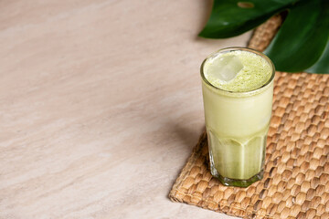 Glasses of matcha latte with coconut milk and white chocolate on marble background. Tropical monstera leaf