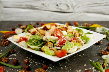 Greek salad on a white square plate. Dark textured background