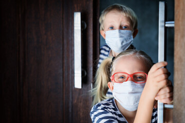 Little children looking out opened door after staying at home due banned street activity. Kids wearing medical face masks go out for outside walk. Ending coronavirus Covid-19 disease quarantine.