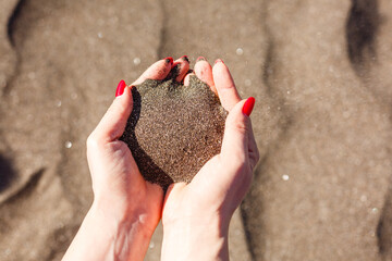 hand pours sand by the sea and rocks. symbol for time running out and time management. nails with manicure.