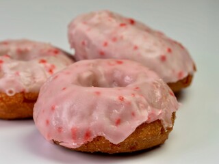 Cherry donuts with pink icing glaze piled up and ready to eat.  Up close still life photography shot of 3 donuts.