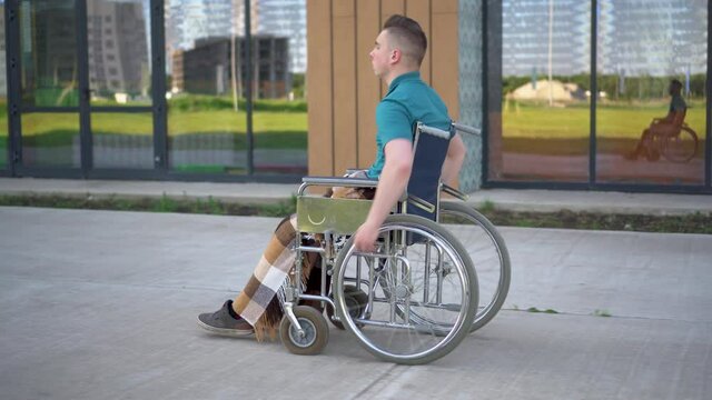Young man in a wheelchair. A man rides in a wheelchair against the background of a glass building. Special transport for the disabled.
