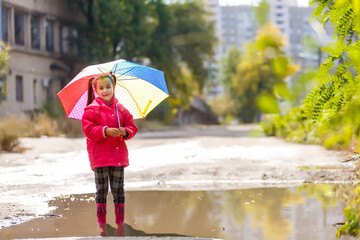 Adorable toddler girl with colorful umbrella outdoors at autumn rainy day