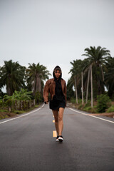 Fototapeta na wymiar Girl in a brown leather jacket is on a paved road with a yellow stripe amongst the palm trees
