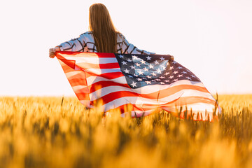Attractive young happy woman, in a wheat field with an American flag on the background of the sunset