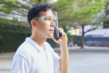 A man is holding a phone outside, wearing a face shield to protect against germs and viruses. Dust prevention and prevention of toxic fumes. Mental Health, Health concept