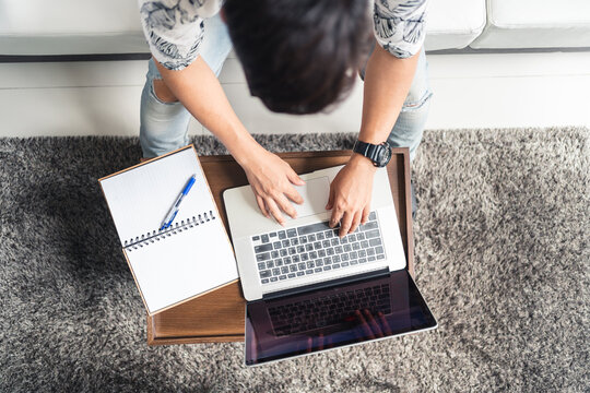 Top View Of Young Asian Man Sitting And Working On Laptop Computer With Notebook For Writing Some Idea. Work From Home Concept.