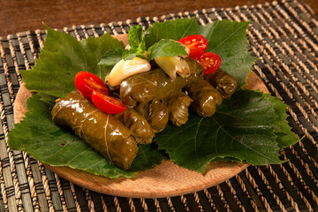 Sarma - Rice and mint wrapped in grape vine leaves on wood background.