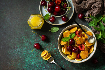 Trendy home breakfast with tiny pancakes cereal. Mini pancakes, honey and cherries on a stone table. Top view flat lay background. Copy space.