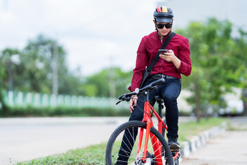 Asian man bicycles to work. He stops and uses his phone.