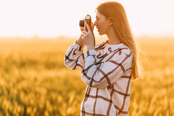beautiful girl with retro camera, on a Golden wheat field against the background of a Sunny sunset