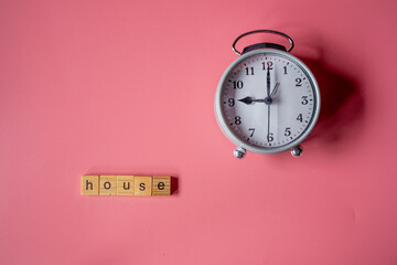 The words "house" made with wooden letters and gray alarm clock on pink background.