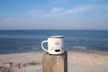 A white cup with a print on the background of the sea, stands on a wooden handrail, Scandinavian motif, sky, mug