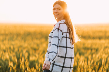 happy woman in a checked shirt strolling through a wheat field during a Sunny sunset