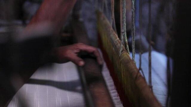Hand of old and poor man weaving cotton threads on big machine at textile factory