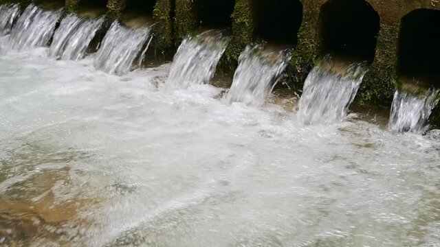 Water flows through pipes inder an old bridge	