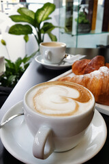 Cup of cappucino with croissant on black table in cafe