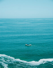 A white tourist boat, sailing through the sea of ​​Puerto Vallarta Jalisco, Mexico, with a turquoise blue sea and a blue sky, with waves bursting near the shore, in a beautiful sunset.