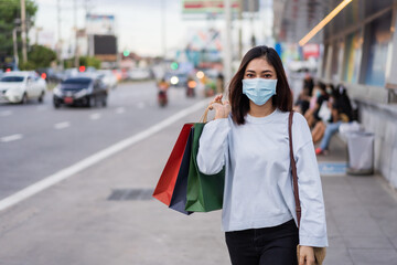 Fototapeta premium woman holding shopping bag at bus stop in city street and wearing face mask protective for spreading of coronavirus(covid-19) pandemic, new normal concept