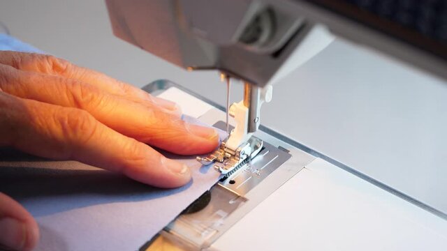 Female hands feeding sewing machine cotton fabric in slow motion. Needle stitching cloth material for a homemade face mask. 