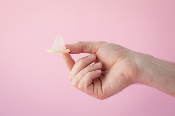 Man's hand holding a condom on a pink background. Contraception concept, prevention of sexually...