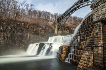 Water cascading down New Croton dam with a bridge arching over the waterfall. 