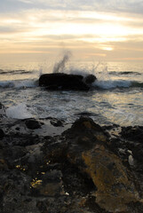 sunset with red and yellow tones, on a beach of yellow stones, with waves crashing on the rocks with a small island in the distance and a cliff behind, in puerto vallarta Jalisco Mexico.