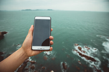 Hand with smartphone on seaside cliff edge