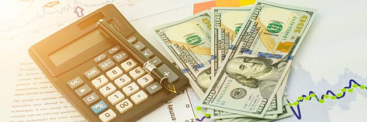 calculator under quill near dollar banknotes on papers