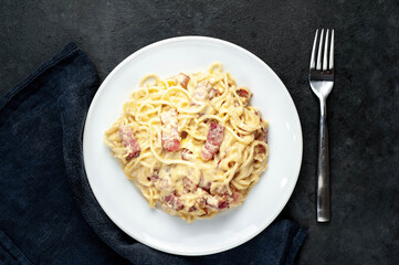 Homemade carbonara pasta in a white plate on a stone background