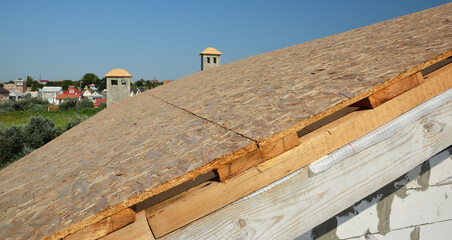 A close-up on roofing construction, roof sheathing with plywood boards, OSB and vapor, damp-proof membrane on roof beams against blue sky.