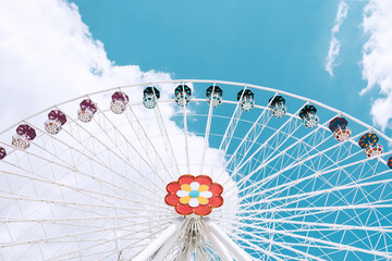 A ferris wheel of white color with multi-colored cabins against the blue sky.